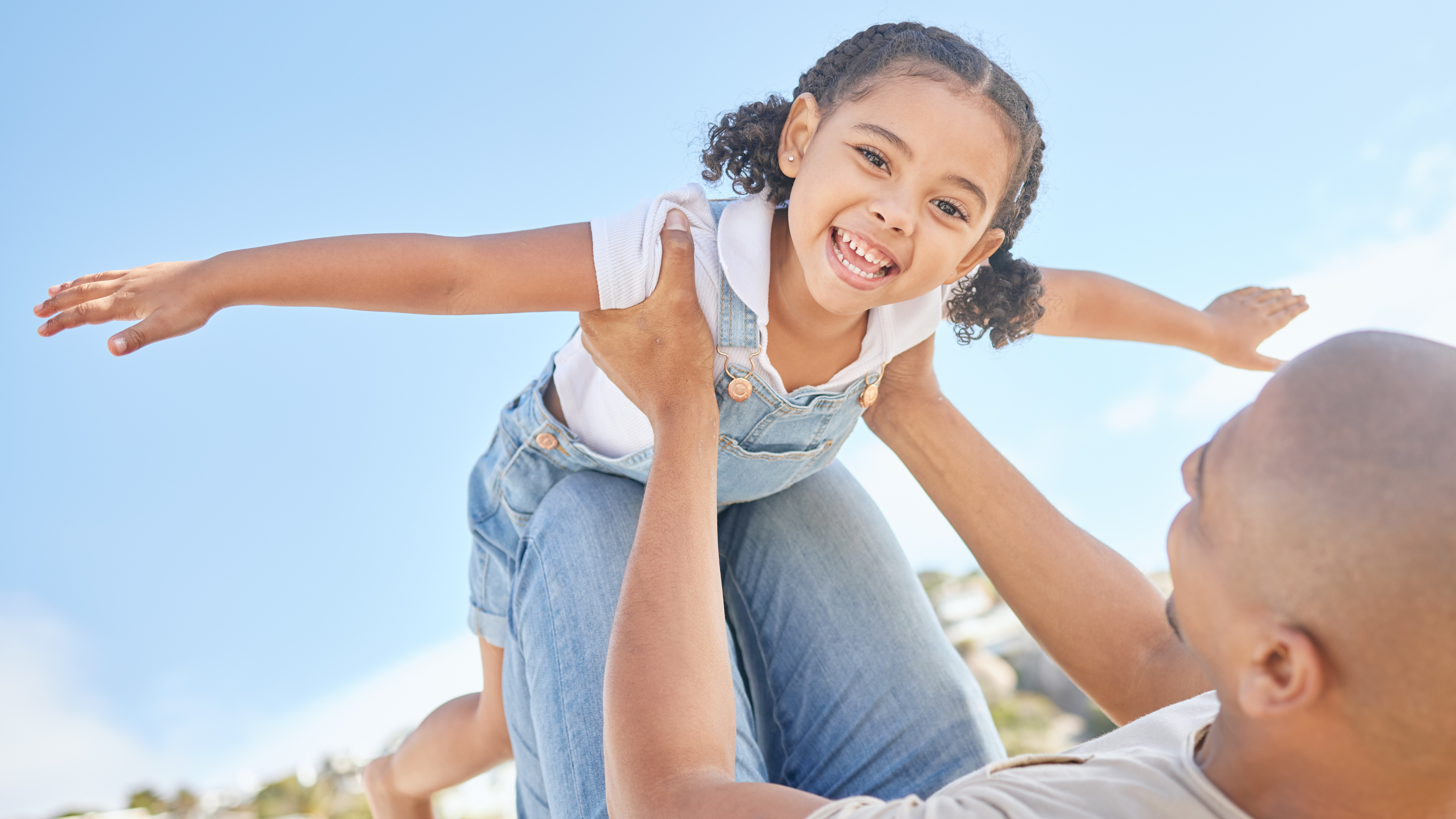 Little girl being lifted in the air by dad. She is pretending to fly. 